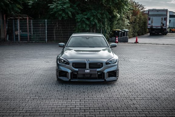 Grauer BMW M2 G87 in Frontansicht mit tiefem Stand und Carbon-Details an der Front.