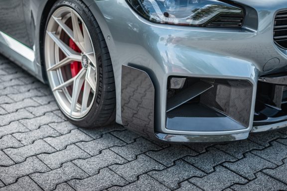 Detail der Front des BMW M2 G87 mit Carbon-Anbauteil, Edelweiss-Vorderrad und rotem Bremssattel.