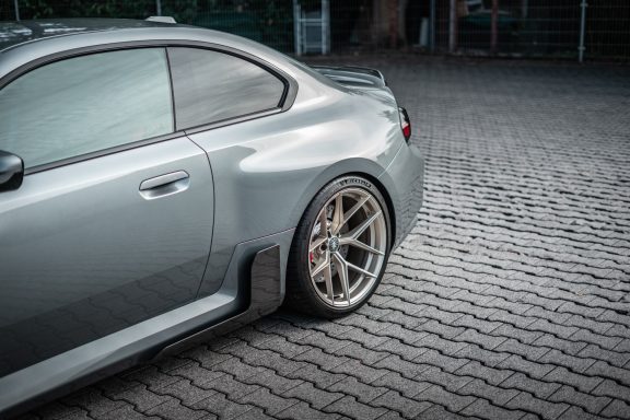 Seitliches Heckdetail des BMW M2 G87 mit Edelweiss-Hinterrad in Champagne und Carbon-Seitenschweller.
