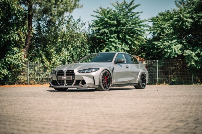 Grauer BMW M3 Competition xDrive G80 schräg von vorn mit schwarzen Yido YP-RS1 und Carbon-Frontspoiler.